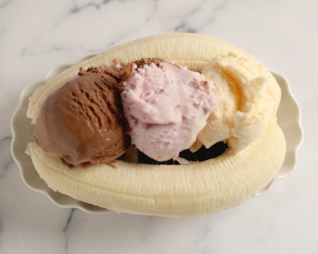 2 slices of a chocolate cake roll with a 2 banana halves and 3 scoops of Neapolitan ice cream on top in a dish