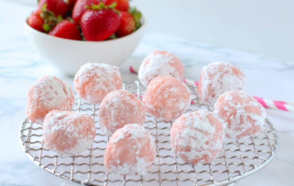 tips for garden party food - Strawberry Cheesecake Cake Balls on circular cooling rack with bowl of strawberries