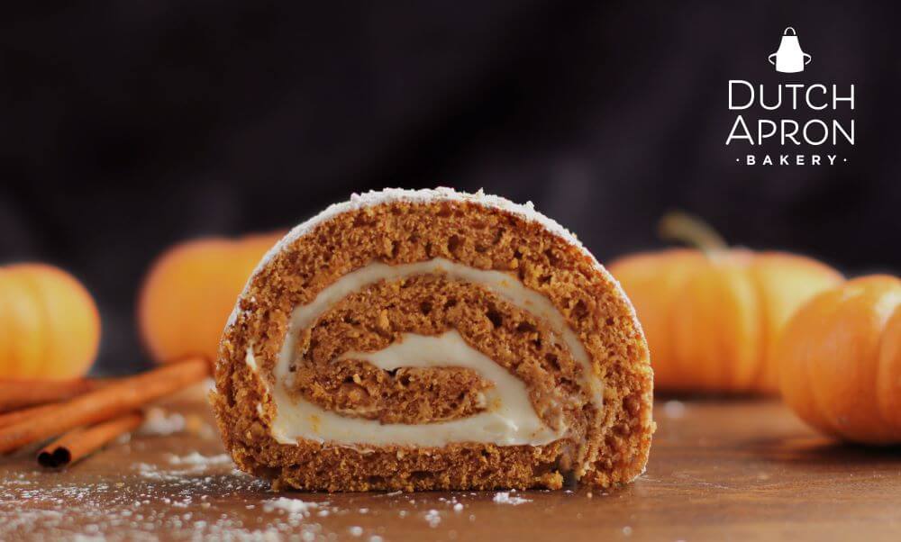 Pumpkin Spice Season - slice of our pumpkin cake roll with pumpkins in background and cinnamon sticks
