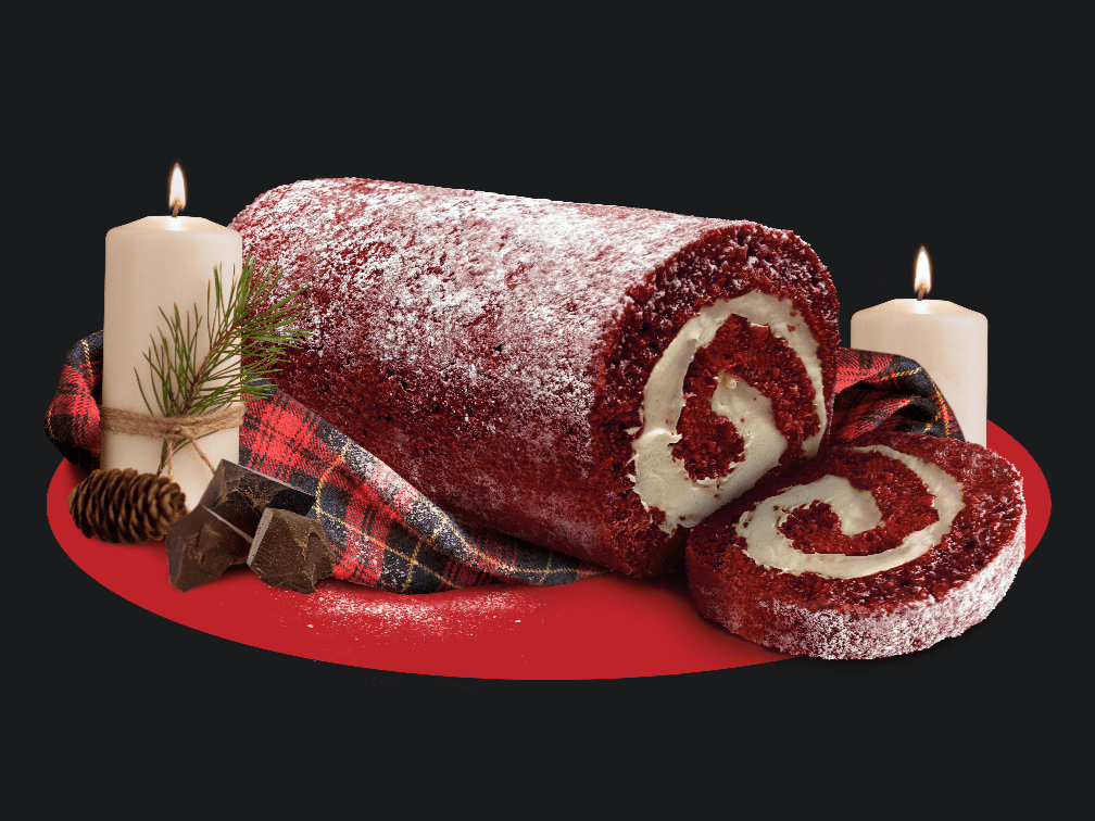 Red Velvet Cake Roll with slice surrounded by candles, chocolate pieces, and flannel cloth