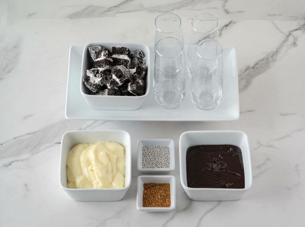 Mini Sparkling Parfait ingredients: cake roll pieces, pudding, fudge, decorations, and glasses
