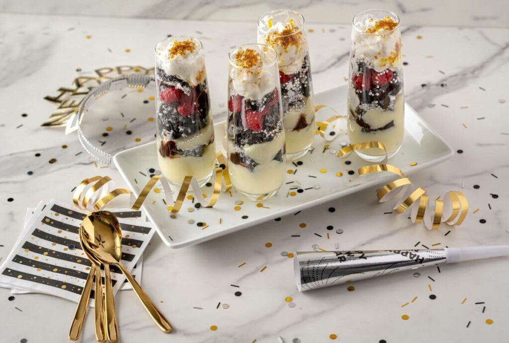 New Year's Eve Desserts - Sparkling Mini Parfaits surrounded by confetti, napkins, spoons, New Year's Eve hat, and noisemaker