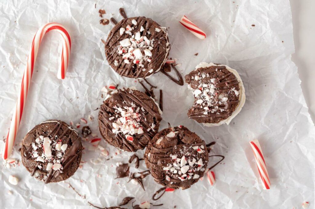 Triple Chocolate Peppermint Cookie Sandwiches next to whole candy cane surrounded by crushed up candy canes