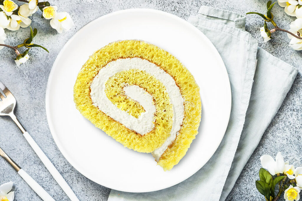 Lemon Crème Cake Roll slice on plate surrounded by white and yellow flowers