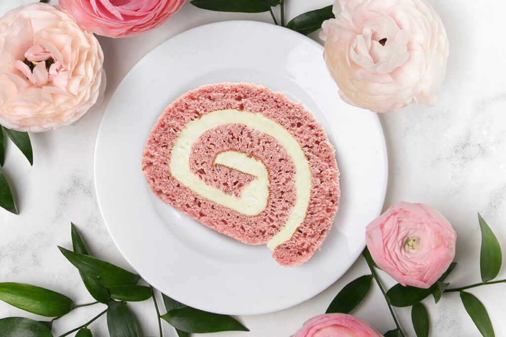 Spring Cake Flavors: Strawberry Cheesecake Cake Roll slice on plate surrounded by pink flowers