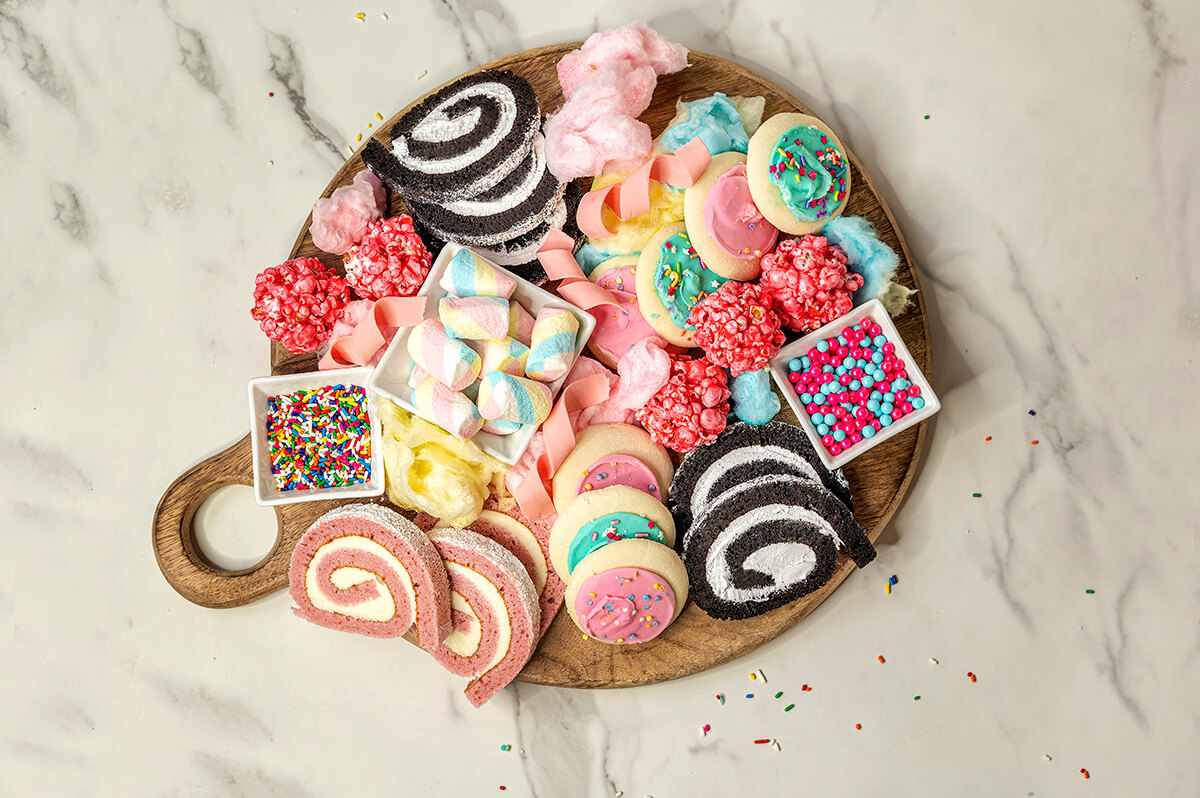 Birthday Cake Charcuterie Board - wooden board with cake roll slices, sprinkles, candies, cookies, popcorn balls, and cotton candy