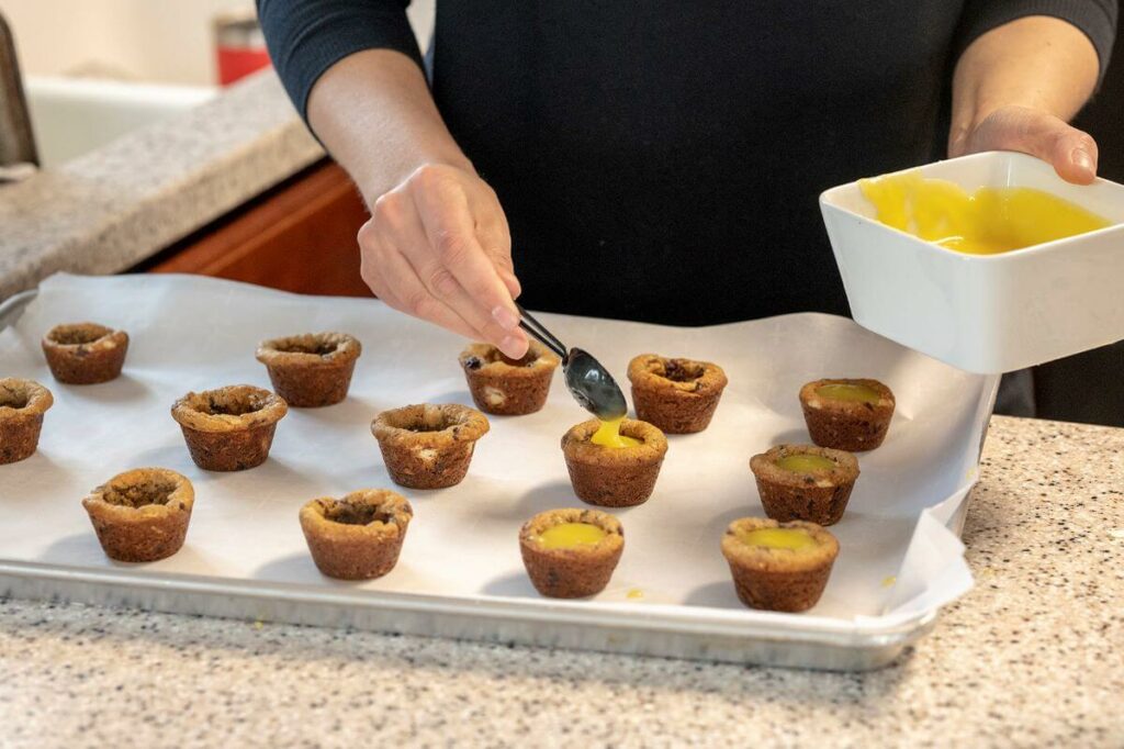 Lemon curd being added to the center of the cookie cups.