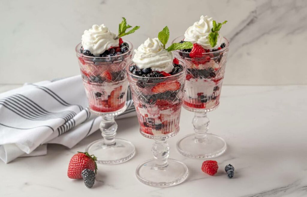 Three glasses of Mixed Berry Shortcakes with berries on the granite table and a cloth napkin.