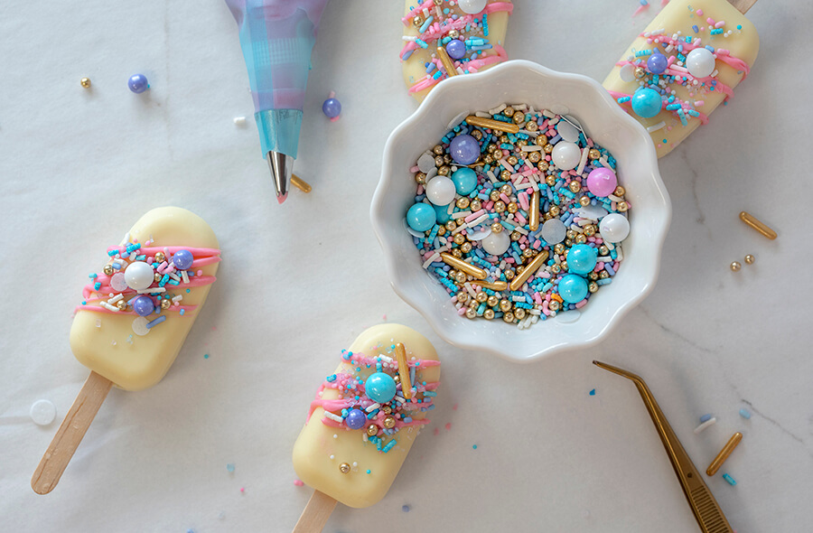 Decorating the cakesicles with colored chocolates and sprinkles