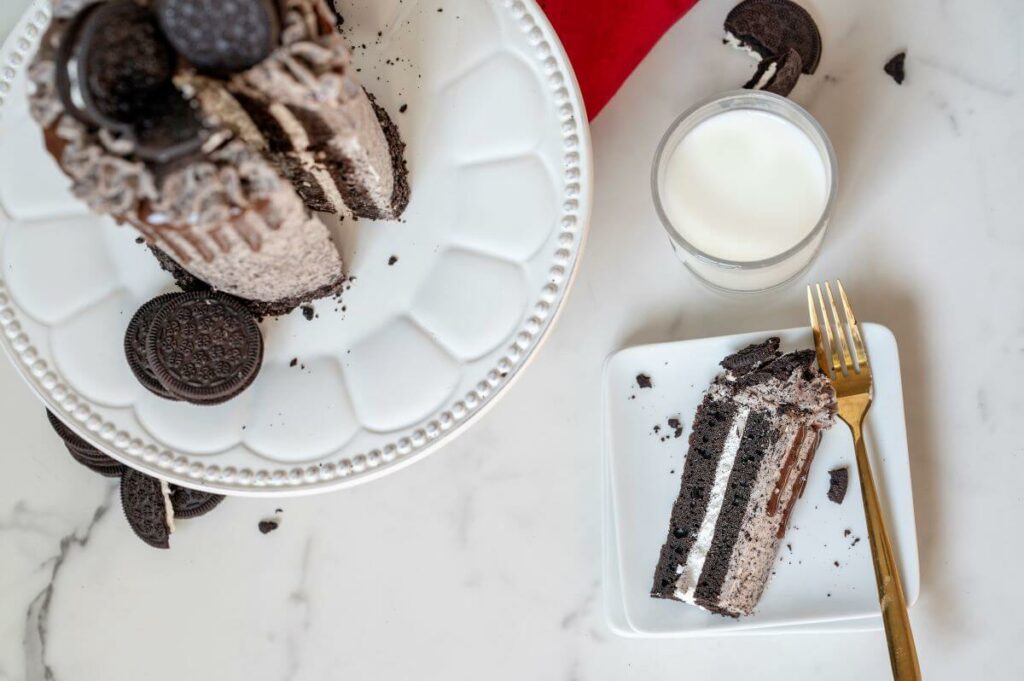 Top down view of the full Cookies and Cream Cake Roll with a slice on a plate next to it and milk, sandwich cookies, and a red napkin in the background.