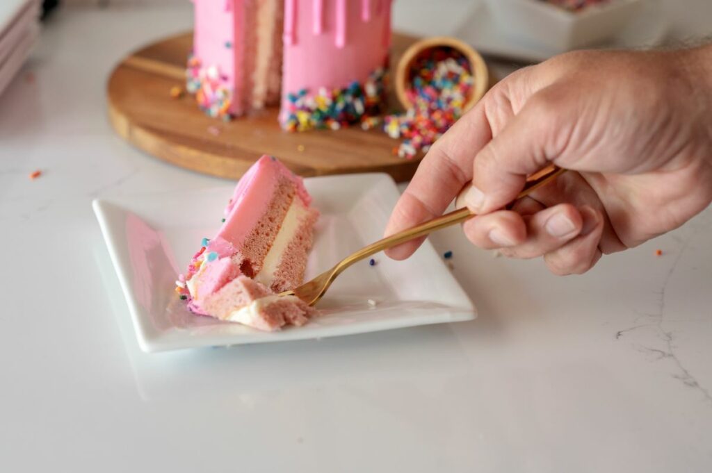 Person grabbing a forkful of cake from a slice of the cake roll that is on the plate. The full Dripping Ice Cream Cone Cake Roll is in the background.