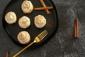 Five Mini Pumpkin Cheesecakes on a plate with cinnamon sticks, sprinkled cinnamon, and a fork.