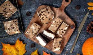 Cappuccino Swirl Bars on a wooden cutting board and two are on a cooling rack. Next to them is a knife. They're surrounded by fall leaves and chocolate pieces.