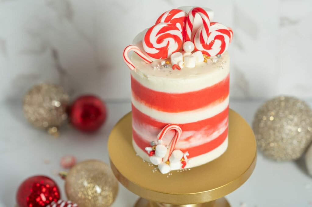 Winter Wonderland Cake Roll on gold cake stand surrounded by red and gold Christmas bulbs.