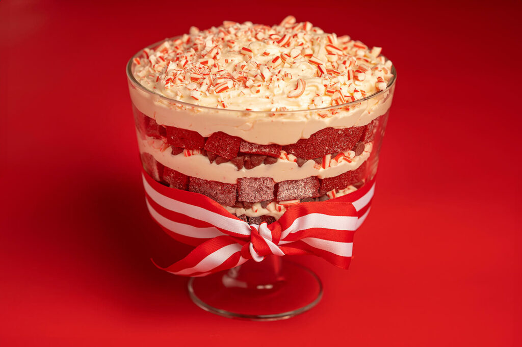Red Velvet Chocolate Peppermint Trifle in trifle bowl with red and white ribbon tied around it, all on a red background.