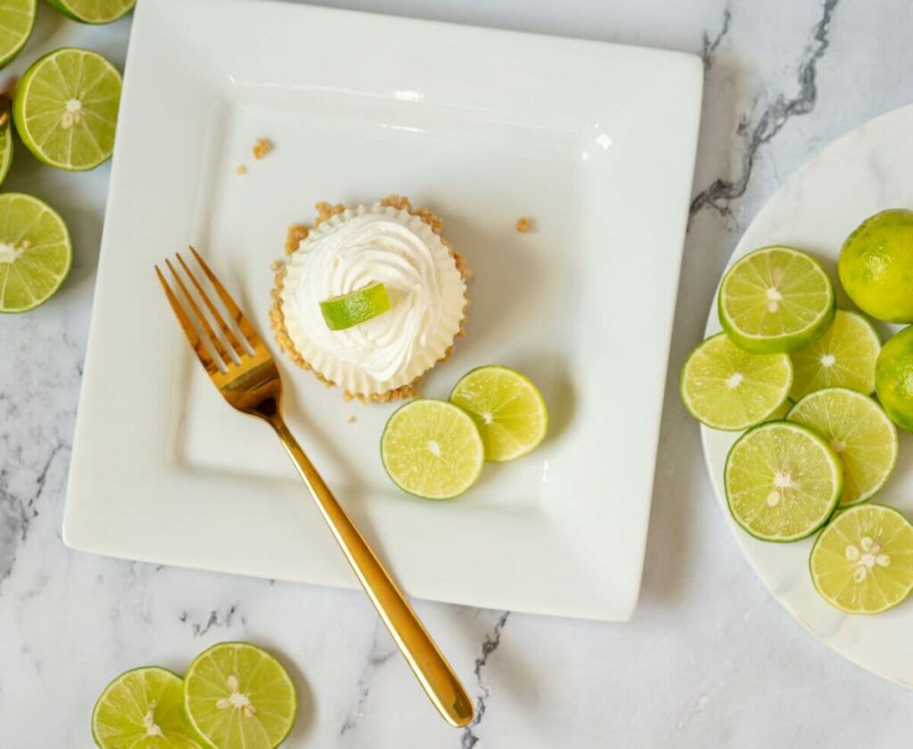 Top down view of one of the key lime pies on a plate. It is surrounded by slices of key limes.