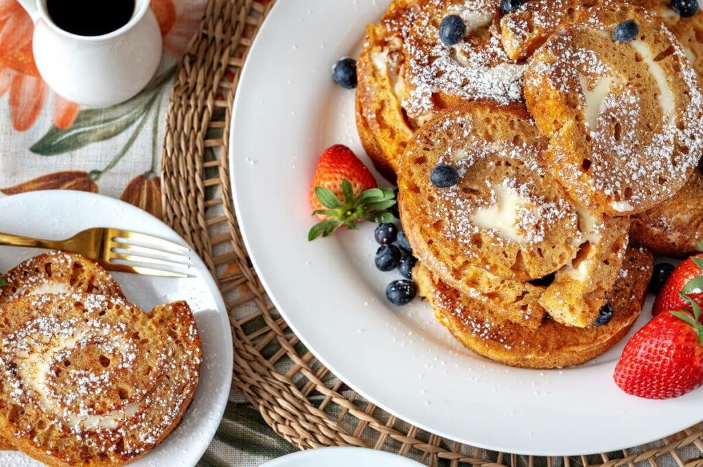 Two plates filled with the French toast slices, covered in powdered sugar and fresh fruit.