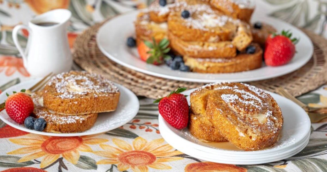 Carrot Cake French Toast - a pile of the French toast on a large plate in the background. Two plates with two slices of French toast each. The slices are covered in powdered sugar and fresh fruit.