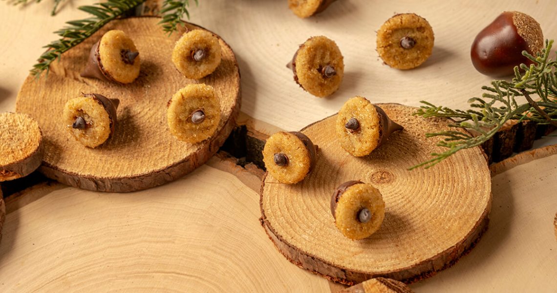 Several Chocolate Peanut Butter Acorn Cookies on serving platters that look like tree stumps surrounded by acorns and fir tree branches.