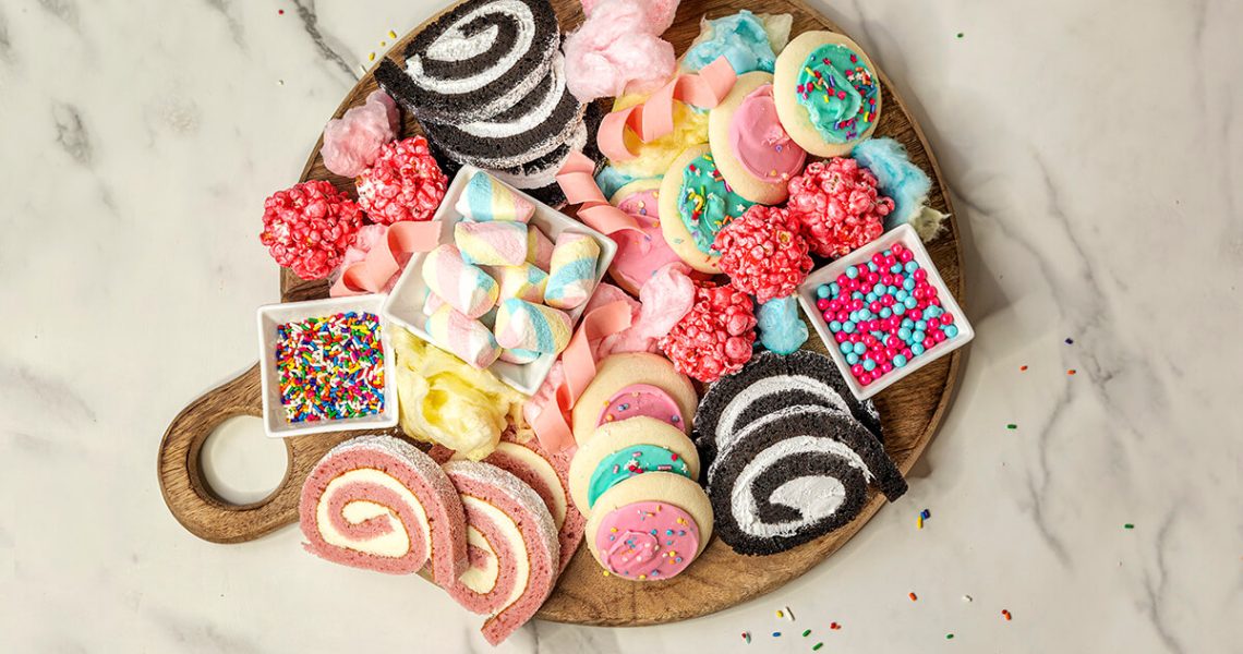 Birthday Cake Charcuterie Board - wooden board with cake roll slices, sprinkles, candies, cookies, popcorn balls, and cotton candy