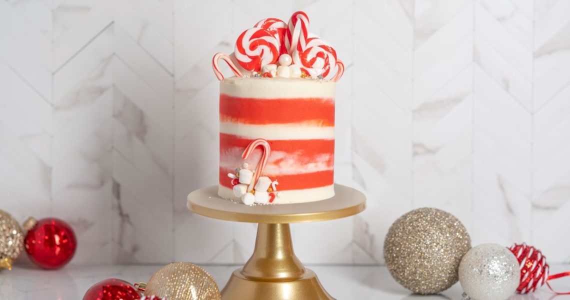 Winter Wonderland Cake Roll on gold cake stand surrounded by red and gold Christmas bulbs.