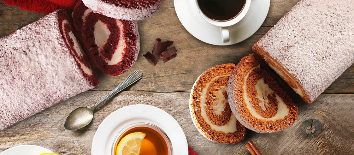 Drink Pairings - Partially cut red velvet and pumpkin cake rolls with 2 white cups and saucers filled with coffee and tea. Spoons, lemons, and cinnamon sticks for garnish on wooden tabletop.