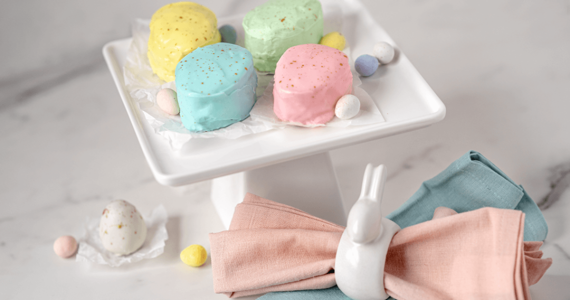 Easter Egg Petit Fours on a cake stand next to napkins in a bunny-shaped napkin holder