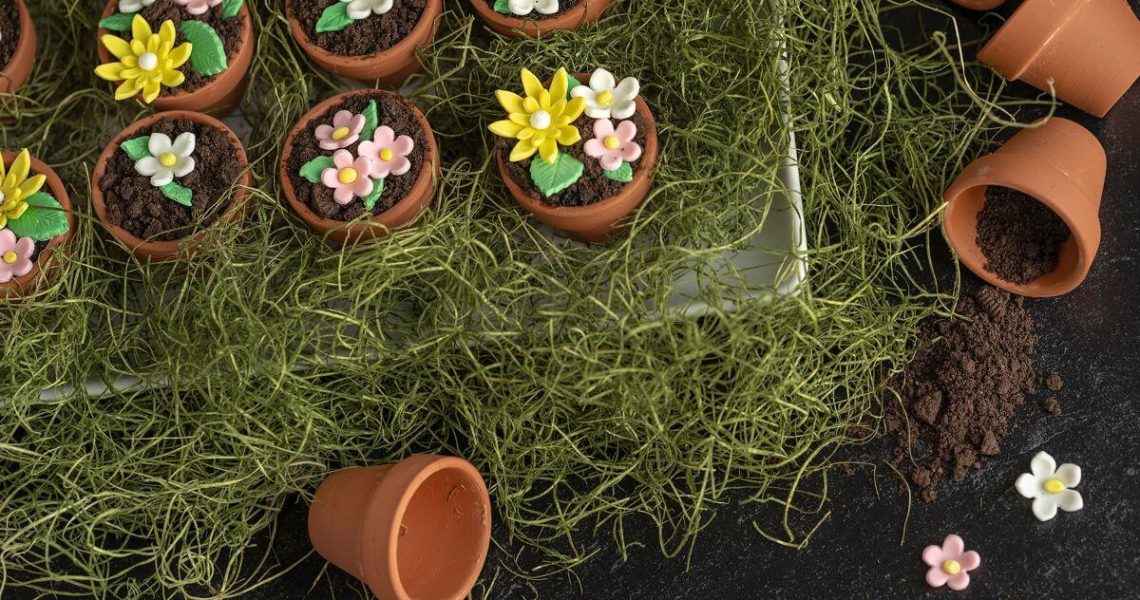 Flowerpot Cakes on a bed of fake grass with several empty flowerpots laying around them, spilling cookie crumb "dirt" and gum paste flowers.
