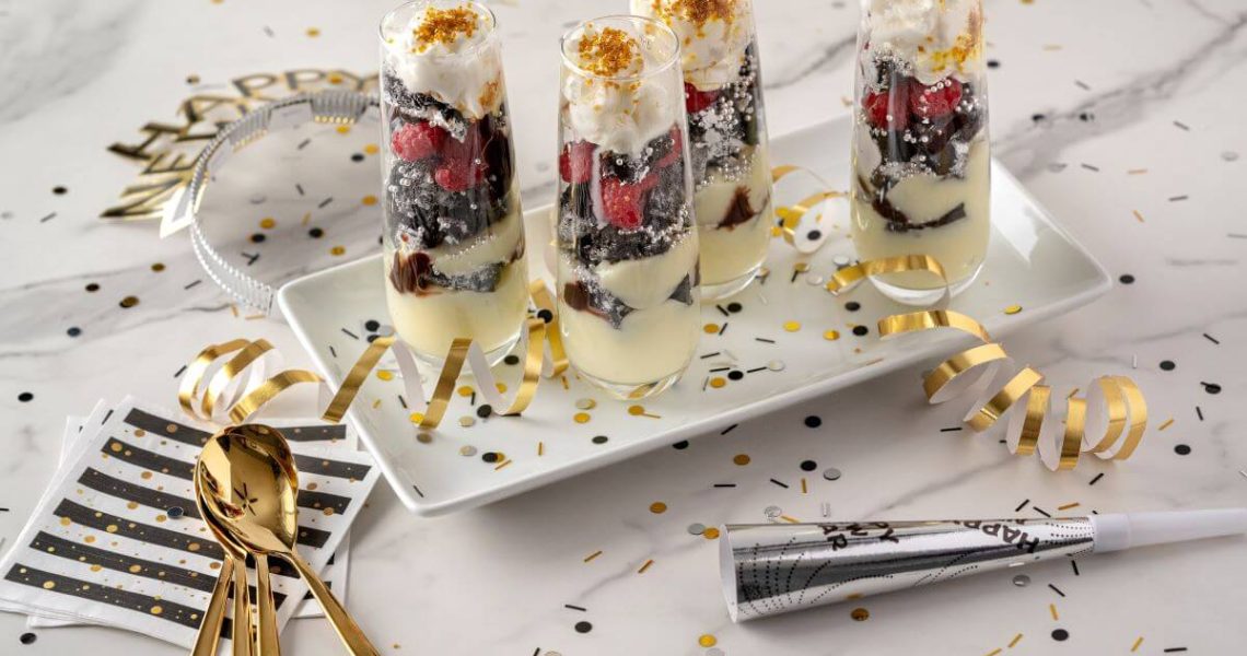 New Year's Eve Desserts - Sparkling Mini Parfaits surrounded by confetti, napkins, spoons, New Year's Eve hat, and noisemaker