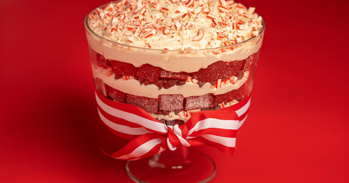 Red Velvet Chocolate Peppermint Trifle in trifle bowl with red and white ribbon tied around it, all on a red background.